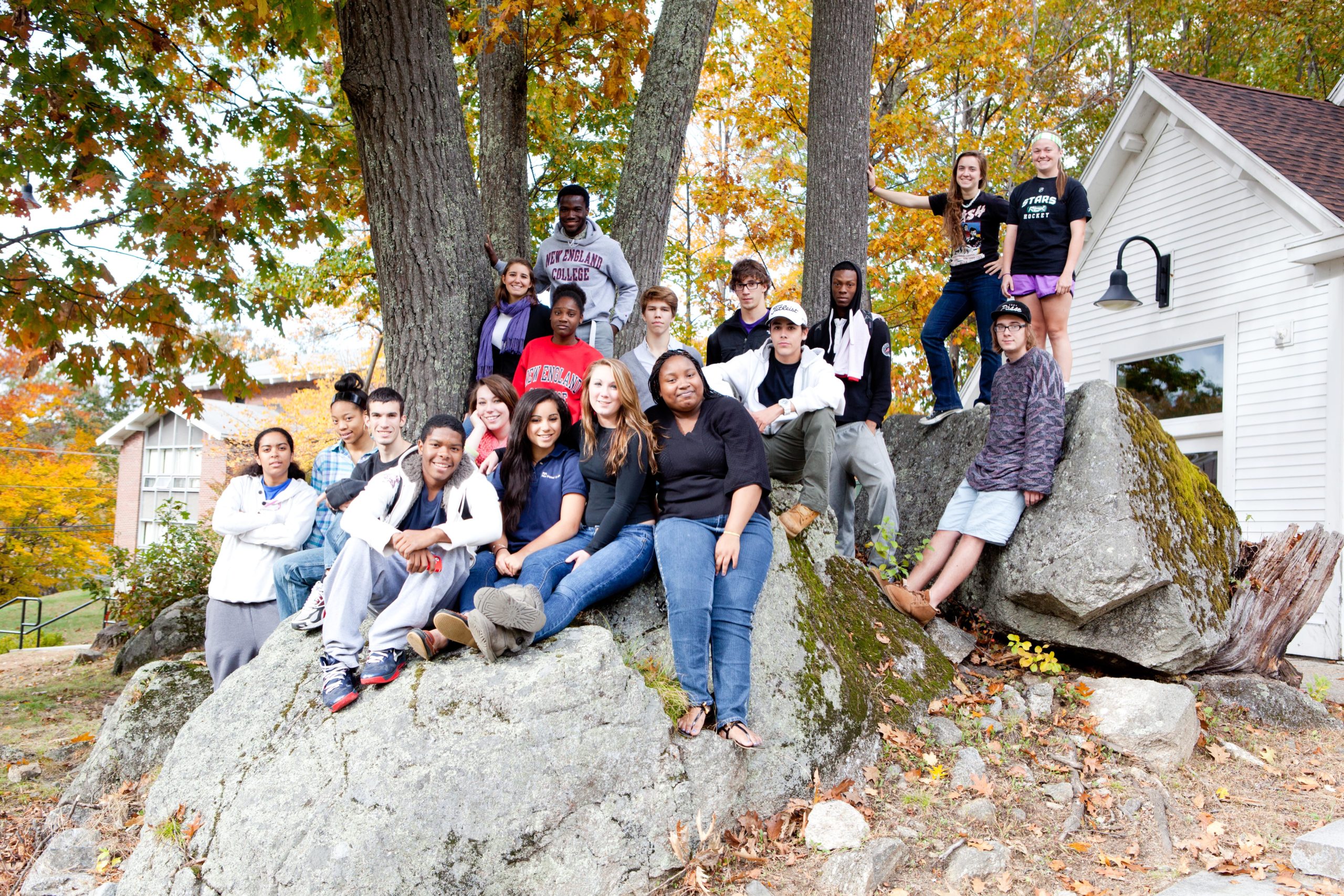 New students sit on a large rock on NEC's Henniker campus