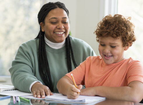 A teacher's assistant helps a young student with his schoolwork.