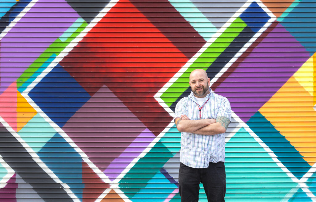 James Chase, Associate Professor at the Institute of Art and Design at NEC, stands in front of one of his Manchester murals.