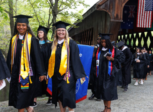 Students walking across the covered bridge for the 2024 Commencement ceremony at New England College