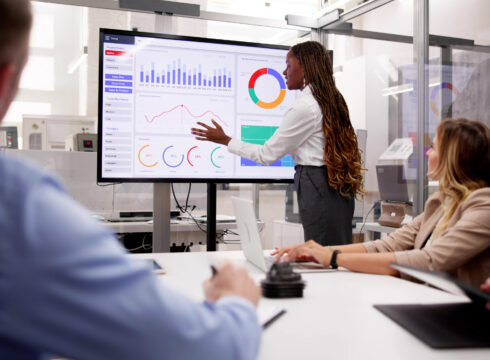An accountant presents financial data on a video screen in a conference room.