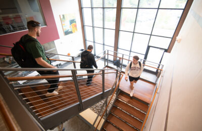 Three students on the stairs in the John Lyons Center at New England College in Henniker, NH