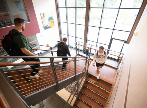 Three students on the stairs in the John Lyons Center at New England College in Henniker, NH