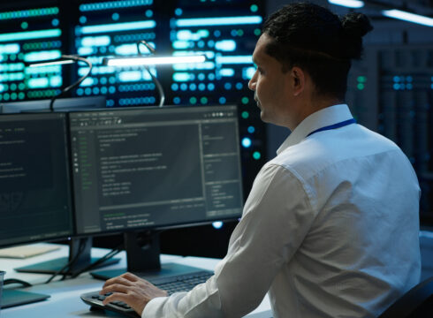 An IT professional in a server room works on a computer.