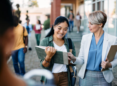 An administrator talks with a student outside a university building.