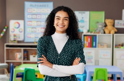 A teacher standing in a classroom and smiling.