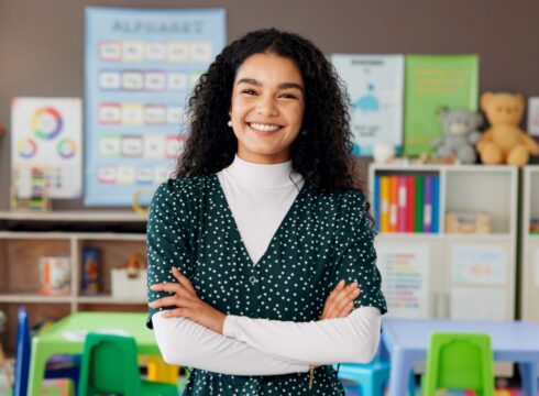 A teacher standing in a classroom and smiling.