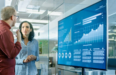 Data scientists review a data visualization dashboard displayed on a smart board.