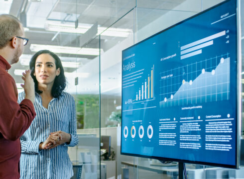 Data scientists review a data visualization dashboard displayed on a smart board.