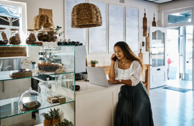 An entrepreneur talks on the phone while using a laptop in her store.