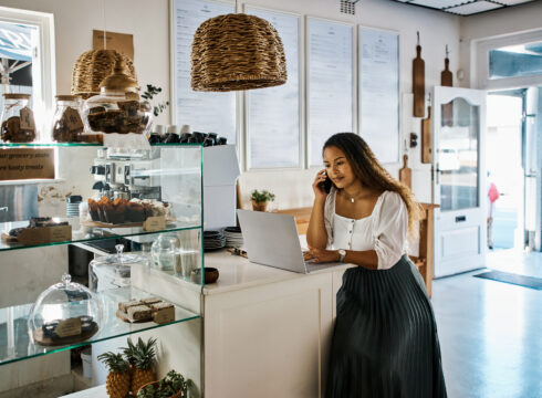 An entrepreneur talks on the phone while using a laptop in her store.
